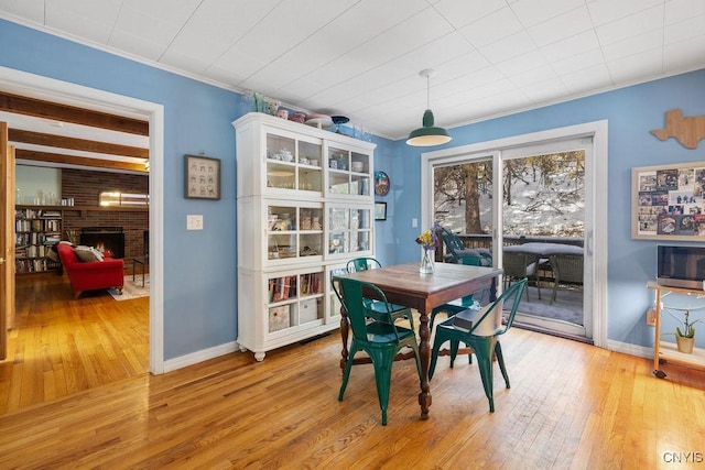 dining room featuring baseboards, crown molding, a brick fireplace, and light wood-style floors