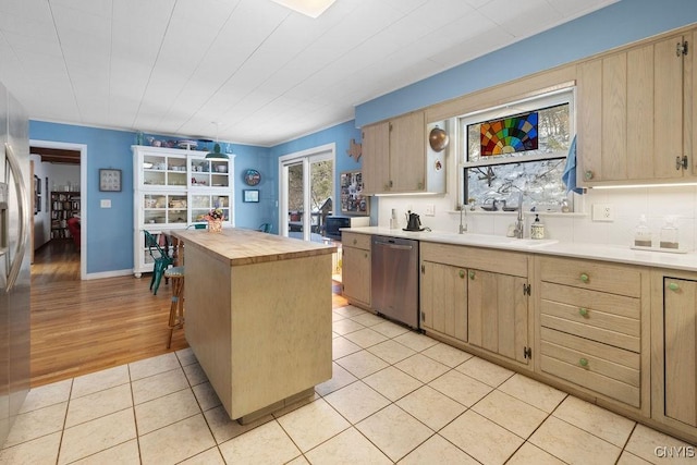 kitchen with light brown cabinets, light tile patterned flooring, wood counters, and stainless steel dishwasher