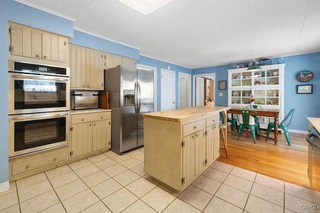 kitchen featuring light tile patterned floors, wood counters, appliances with stainless steel finishes, ornamental molding, and a center island