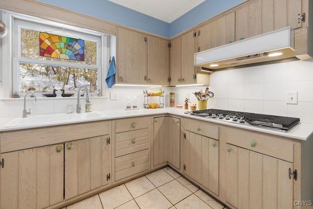 kitchen featuring under cabinet range hood, stainless steel gas cooktop, a sink, light countertops, and decorative backsplash