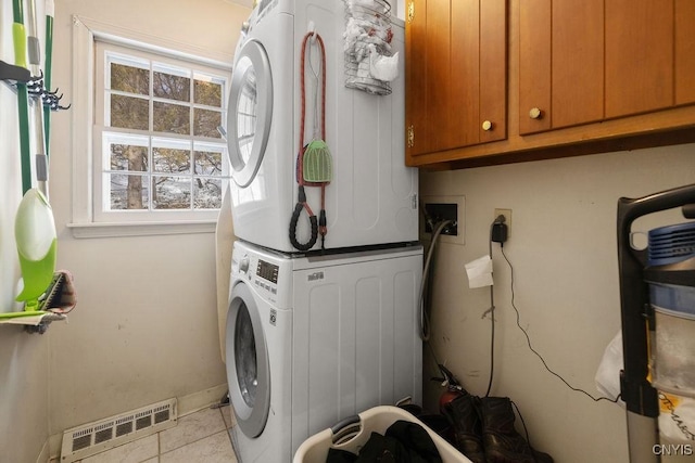 laundry room with stacked washer and dryer, tile patterned flooring, visible vents, and cabinet space