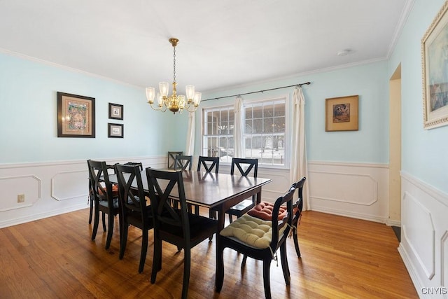 dining space with wainscoting, an inviting chandelier, light wood-style flooring, and crown molding