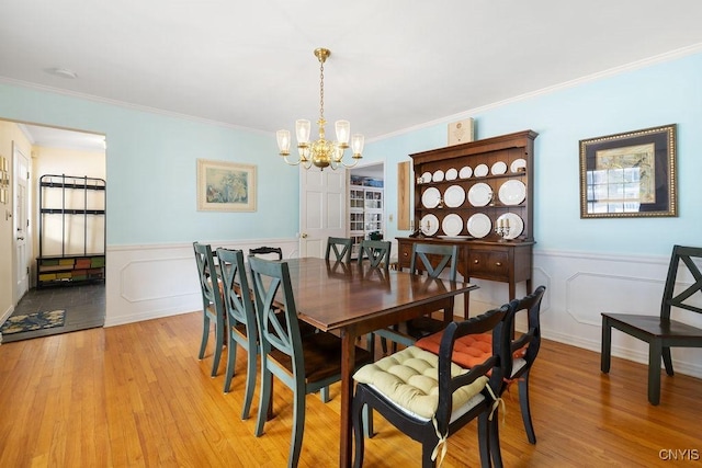 dining area featuring a chandelier, wainscoting, ornamental molding, and light wood-style flooring