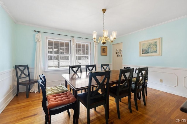 dining room with ornamental molding, wainscoting, a notable chandelier, and light wood-style flooring