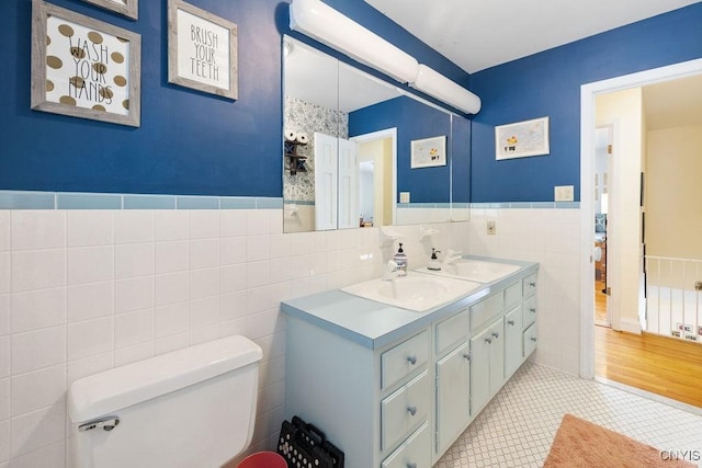 full bathroom featuring toilet, a wainscoted wall, a sink, tile walls, and tile patterned floors