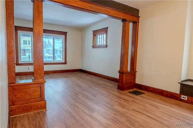 unfurnished room with visible vents, wood finished floors, decorative columns, and baseboards