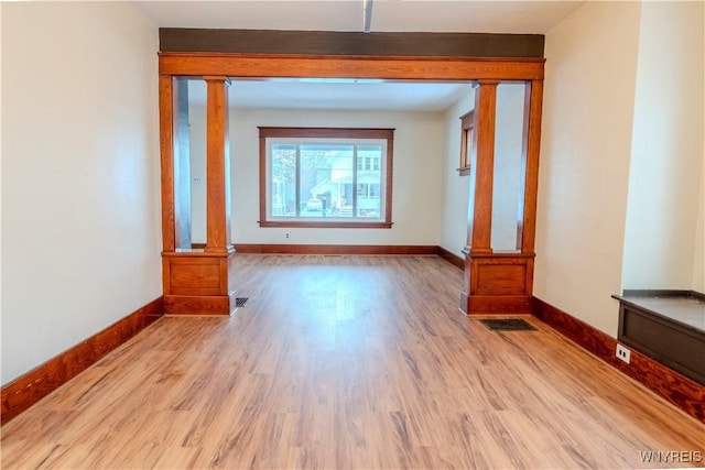 unfurnished room with baseboards, visible vents, ornate columns, and wood finished floors