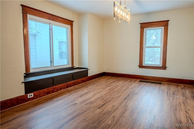 spare room featuring a notable chandelier, wood finished floors, visible vents, and baseboards