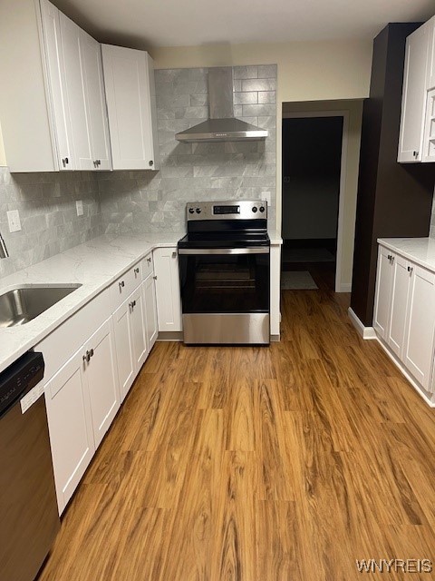 kitchen featuring stainless steel appliances, a sink, white cabinetry, wall chimney range hood, and light wood finished floors