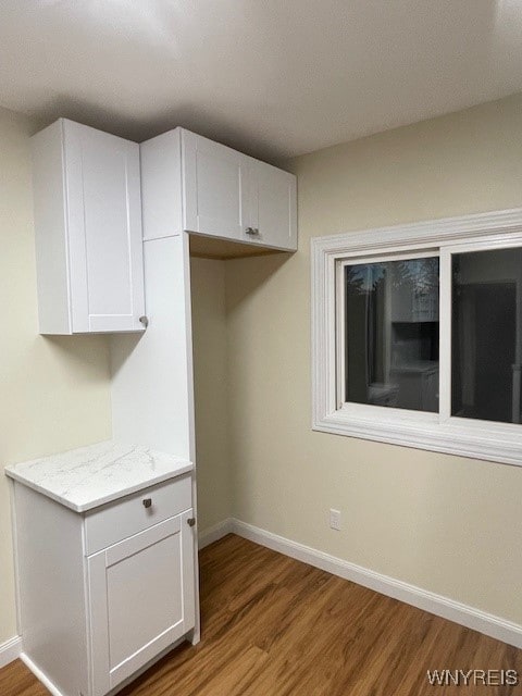 interior space with light wood finished floors, baseboards, white cabinets, and light stone counters