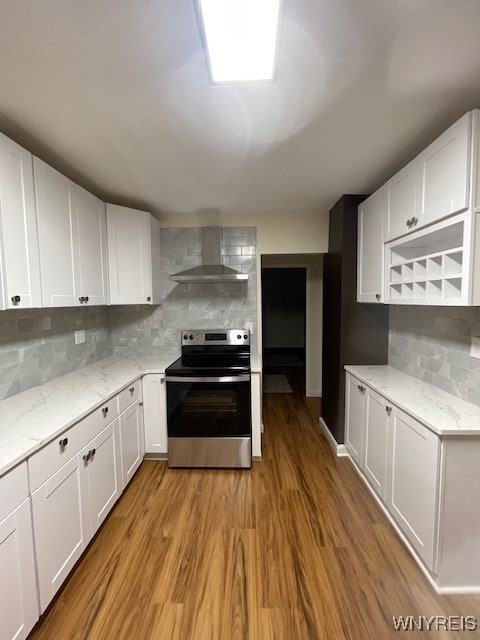 kitchen with tasteful backsplash, light wood-style flooring, stainless steel range with electric cooktop, wall chimney range hood, and white cabinetry