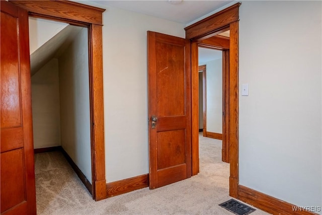 corridor with baseboards, visible vents, and light colored carpet