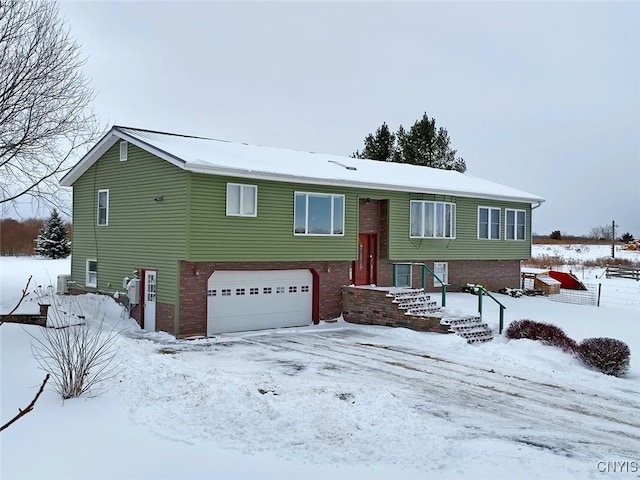 bi-level home featuring an attached garage, central AC unit, and brick siding