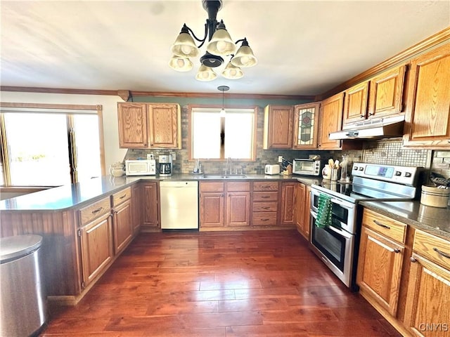 kitchen with white appliances, decorative backsplash, a peninsula, under cabinet range hood, and a sink