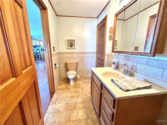 bathroom with toilet, vanity, wainscoting, stone finish floor, and crown molding