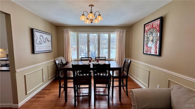 dining space with dark wood-style floors, a decorative wall, a wainscoted wall, and an inviting chandelier