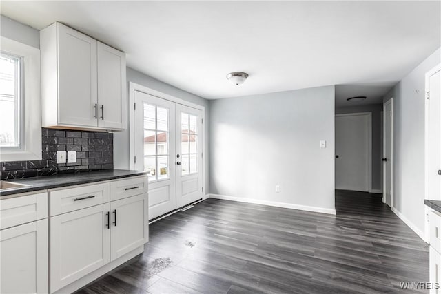 kitchen with baseboards, white cabinets, decorative backsplash, dark countertops, and dark wood finished floors