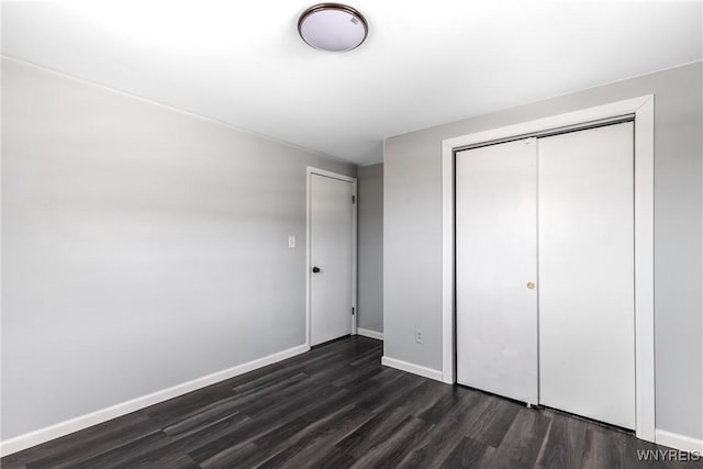 unfurnished bedroom with a closet, dark wood finished floors, and baseboards