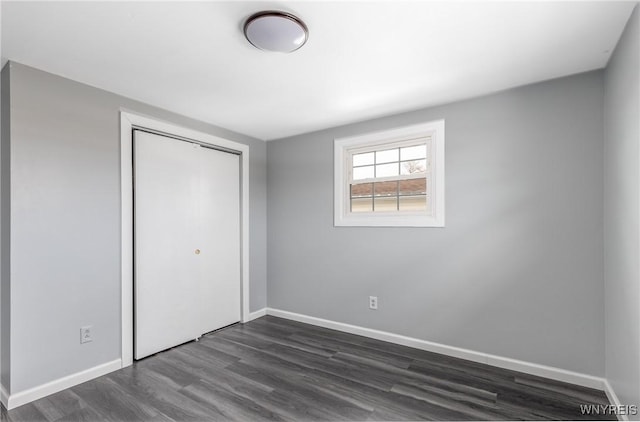 unfurnished bedroom featuring baseboards, dark wood finished floors, and a closet