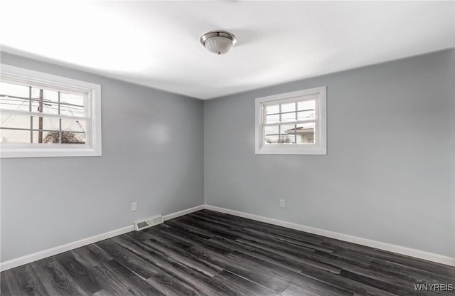 empty room featuring dark wood-style floors, baseboards, and visible vents