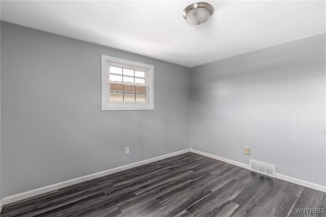 unfurnished room featuring dark wood-style flooring, visible vents, and baseboards