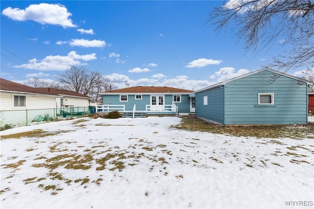 snow covered back of property featuring french doors, a detached garage, and fence