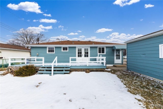 snow covered house with a deck and french doors