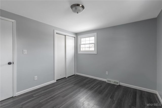 unfurnished bedroom featuring dark wood-style flooring, a closet, visible vents, and baseboards