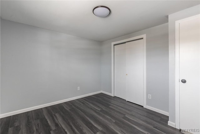 unfurnished bedroom with a closet, dark wood finished floors, and baseboards