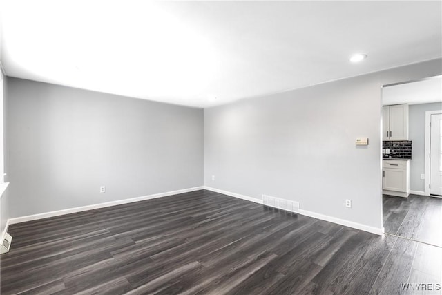 empty room featuring dark wood-style floors, recessed lighting, visible vents, and baseboards