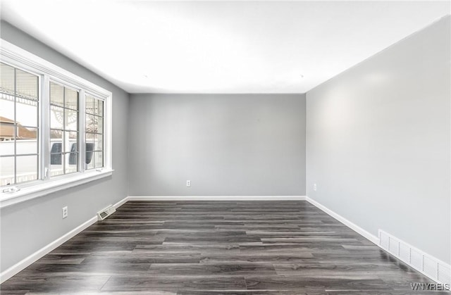 empty room featuring dark wood finished floors, visible vents, and baseboards