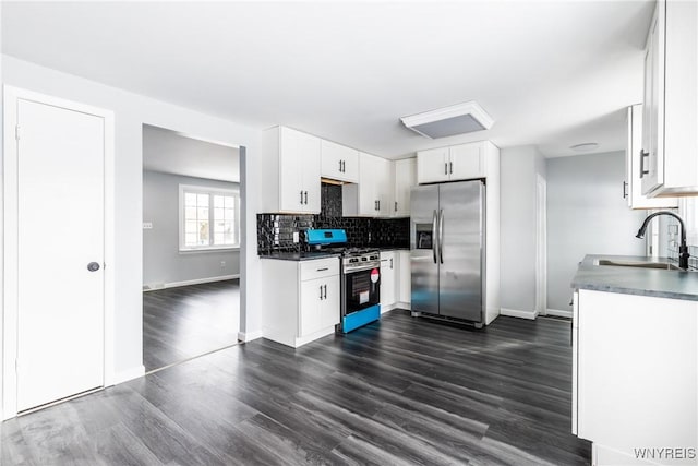 kitchen featuring dark wood finished floors, stainless steel appliances, dark countertops, backsplash, and a sink