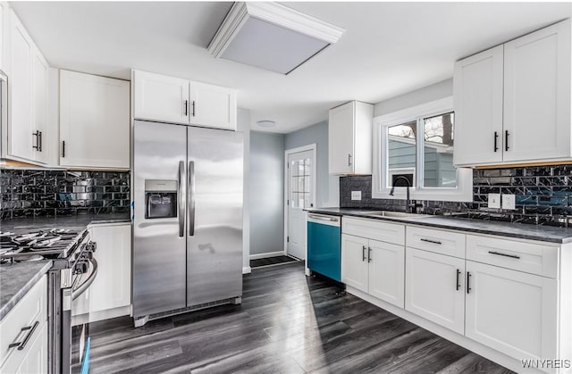 kitchen with dark wood-style flooring, stainless steel appliances, dark countertops, white cabinets, and a sink