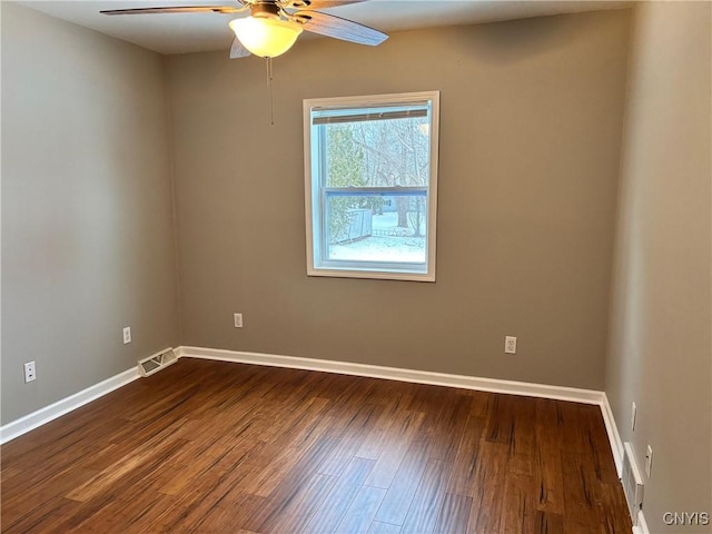 spare room featuring dark wood-style floors, a ceiling fan, visible vents, and baseboards