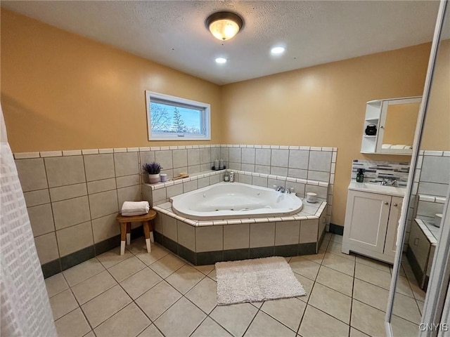 full bath with a textured ceiling, tile walls, vanity, tile patterned floors, and a whirlpool tub