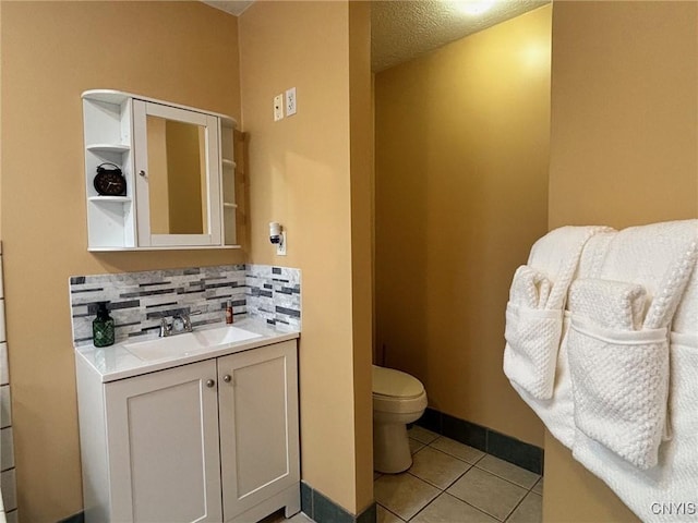 bathroom featuring tile patterned flooring, toilet, vanity, baseboards, and decorative backsplash