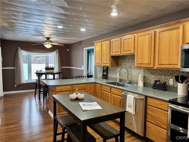 kitchen with stainless steel appliances, a peninsula, dark wood-style flooring, a sink, and tasteful backsplash