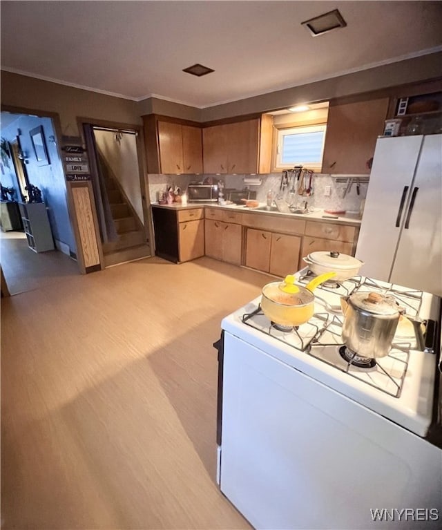 kitchen with decorative backsplash, ornamental molding, light countertops, white range, and light brown cabinets