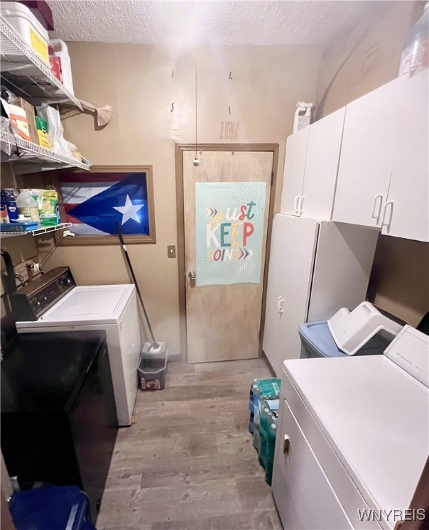 laundry room featuring light wood-style floors, cabinet space, a textured ceiling, and washing machine and clothes dryer