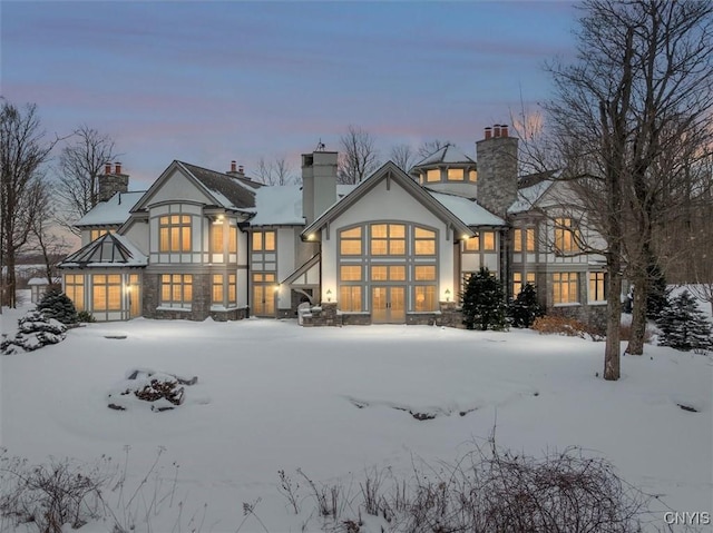 snow covered back of property with stone siding, a chimney, and stucco siding