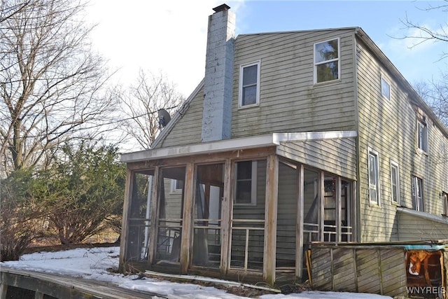 view of snow covered exterior with a sunroom and a chimney