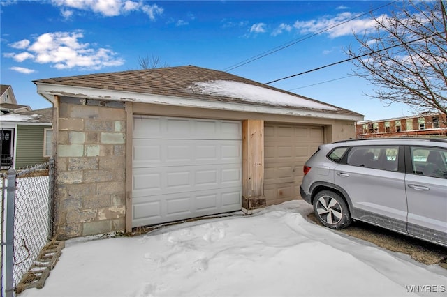 snow covered garage featuring a detached garage and fence