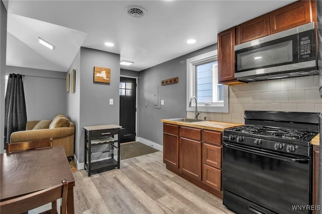 kitchen featuring black range with gas cooktop, decorative backsplash, stainless steel microwave, light wood-type flooring, and a sink