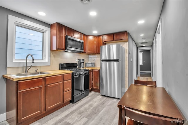 kitchen with tasteful backsplash, light countertops, light wood-style flooring, appliances with stainless steel finishes, and a sink