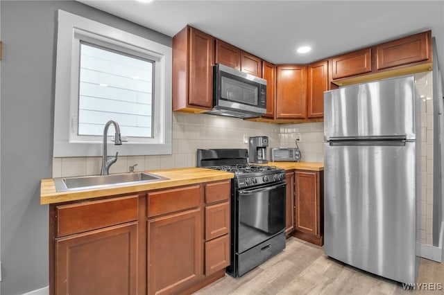 kitchen featuring decorative backsplash, appliances with stainless steel finishes, light wood-type flooring, wooden counters, and a sink