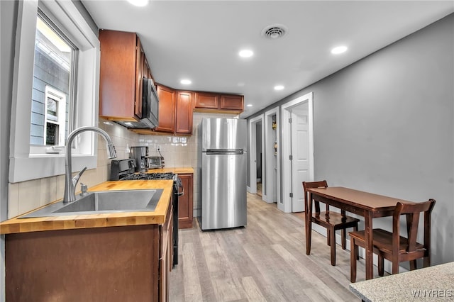 kitchen featuring light wood-style flooring, appliances with stainless steel finishes, backsplash, wooden counters, and a sink