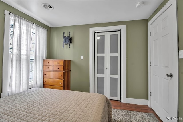 bedroom with a closet, visible vents, dark wood finished floors, and baseboards