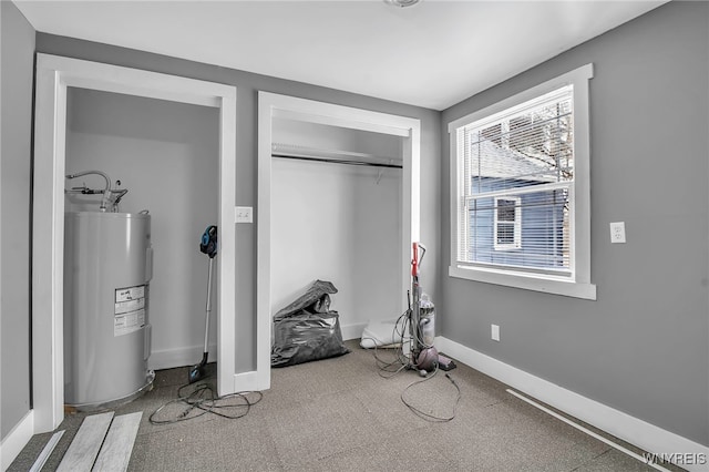 exercise area featuring carpet, water heater, and baseboards