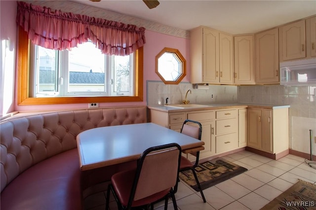 kitchen with light tile patterned floors, a sink, light countertops, cream cabinetry, and decorative backsplash