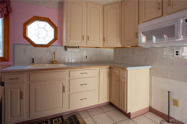 kitchen featuring white microwave, a sink, light countertops, backsplash, and light tile patterned flooring